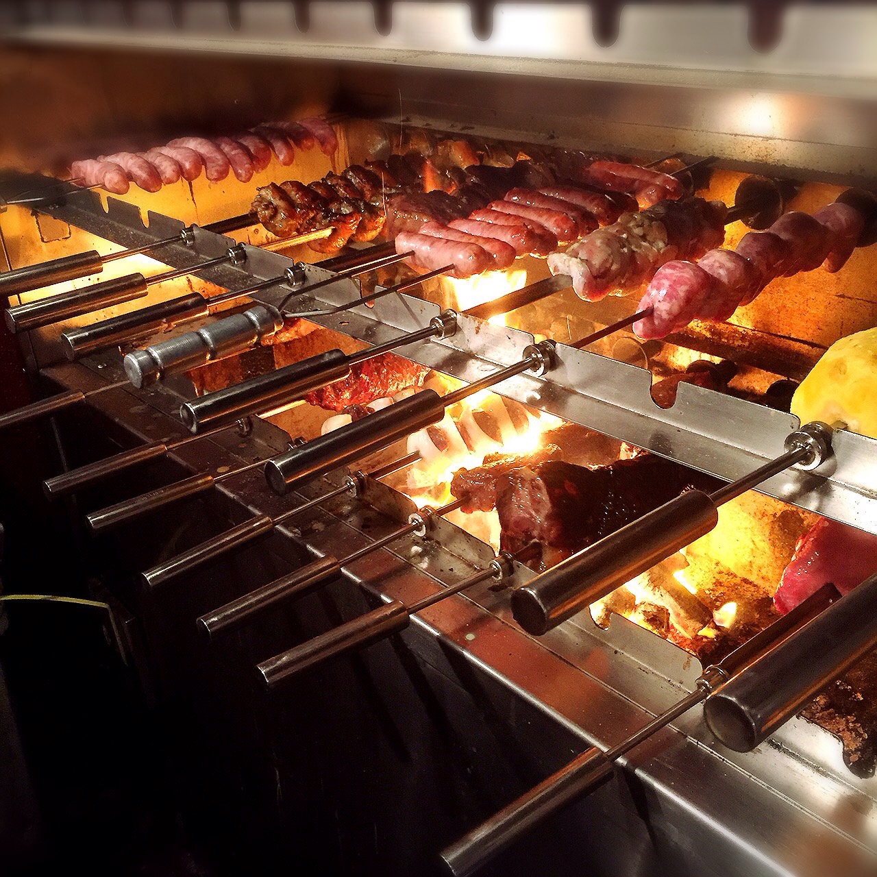 炭火の上で回る何本もの串。ソーセージ、牛肉、鶏肉、パイナップルがステンレスの炉の中で焼けていく。