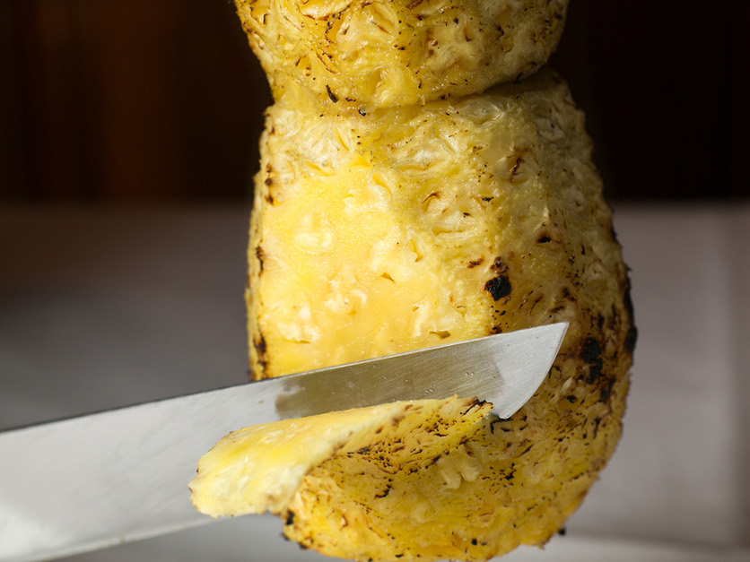 串に刺した焼きパイナップルを長いナイフで削ぎ切りにするところ。
