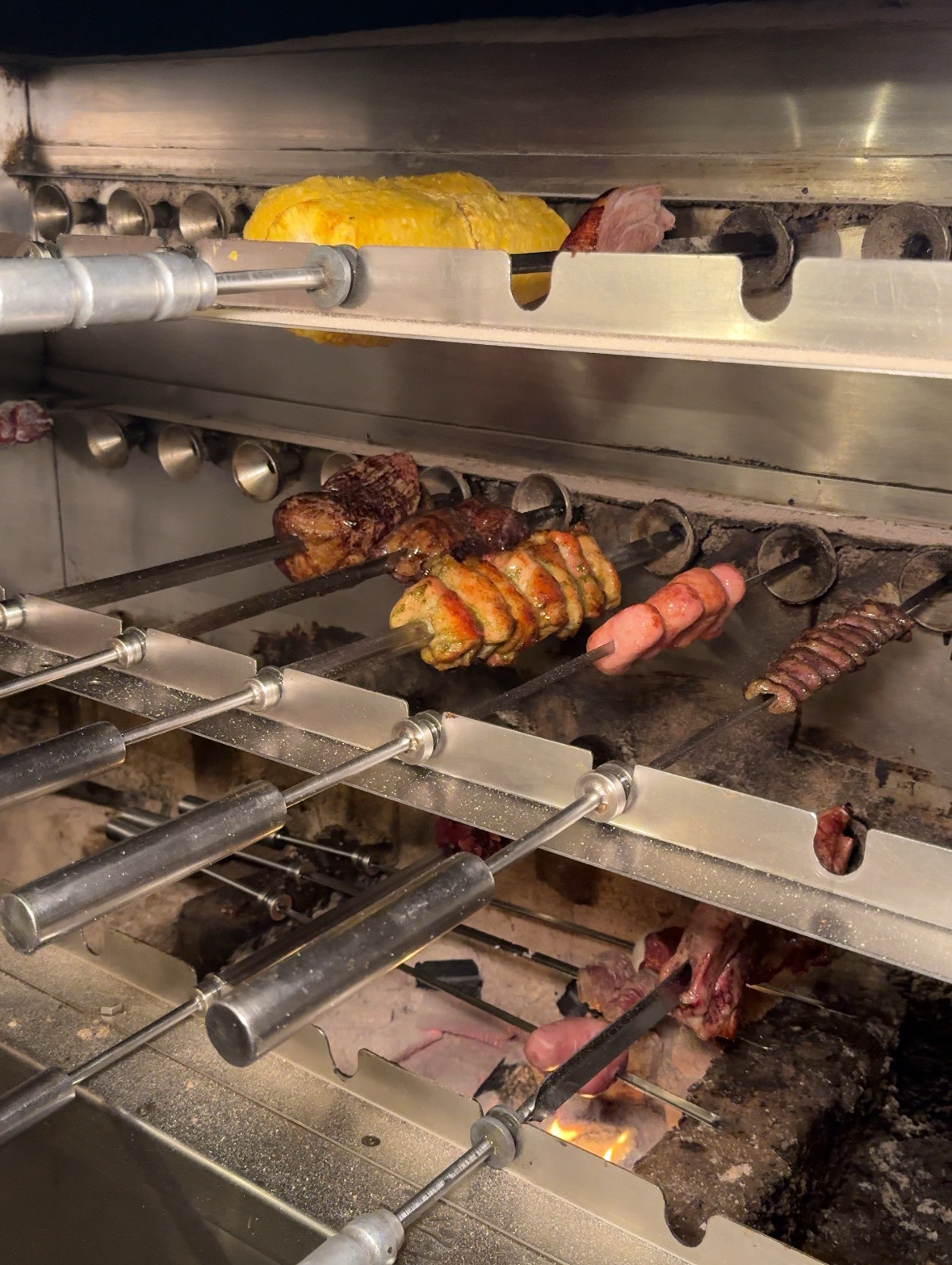横から見た炭火の焼き台。パイナップル、鶏肉、ソーセージ、牛肉の串が並ぶ。